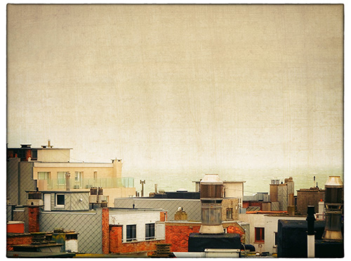 This picture belongs to the series "the coast". In the foreground house roofs. In the background the sea.