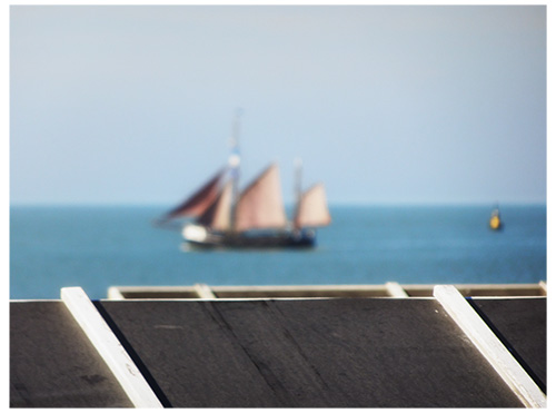 This picture belongs to the series "the coast". In the background a sailing ship on the blue sea. In the foreground the roof of many beach chairs.